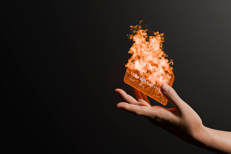 Hand holds credit card wrapped in flames on black background with copy space. Compulsive shopping concept. 3d rendering.の写真素材