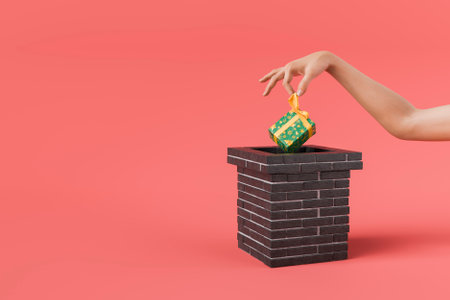 Hand placing a christmas gift in a chimney on a red background. Concept of winter celebration and the spirit of giving. 3d renderingの写真素材