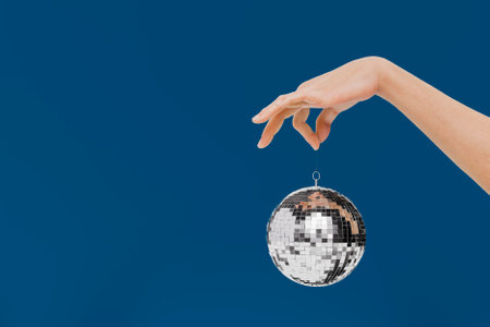 Hand holding a mini disco ball as a christmas ornament on blue background. 3d rendering.の写真素材