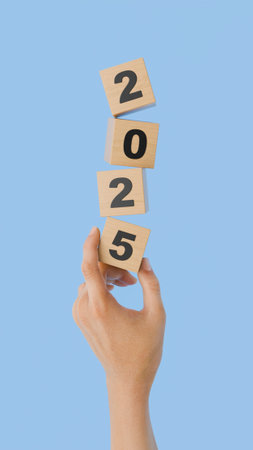 Hand carefully balancing wooden cubes forming the number 2025 against a blue background. 3d renderingの写真素材