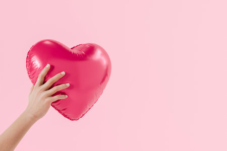 Hand holding a pink heart shaped balloon on a pink background, celebrating love and affection for Valentine's day. 3d renderingの写真素材