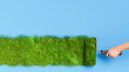 Hand using a paint roller painting green grass on a blue background, symbolizing spring and environmental concepts. 3d renderingの写真素材