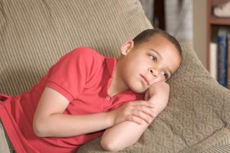 sad looking young boy resting alone on the couchの写真素材
