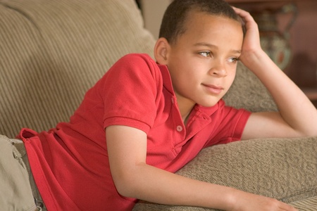 elementary school aged boy laying on couch staring into distanceの写真素材
