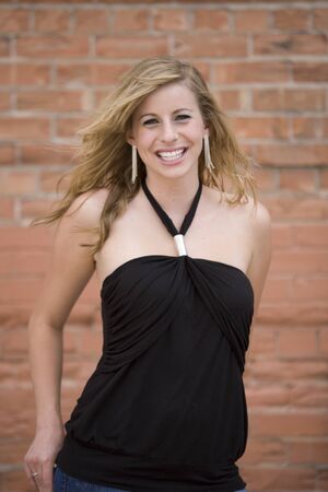 casual smiling blonde woman in front of brick wallの写真素材