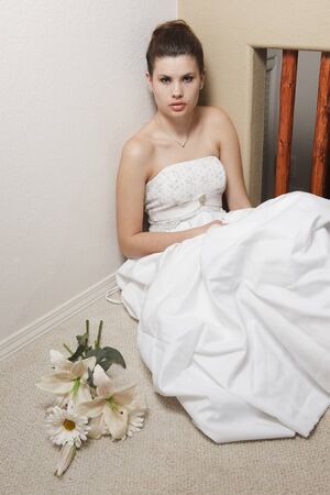 Nervous young woman wearing a wedding gown, sitting on an interior floor の写真素材