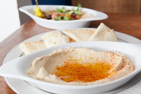Plate of hummus covered with oil that has a salad in the backgroundの写真素材