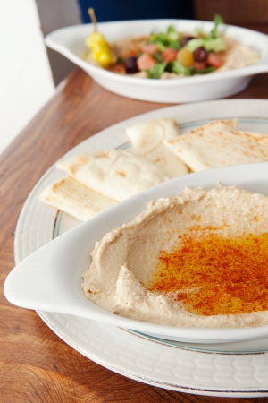 Plate of hummus covered with oil that has a salad in the backgroundの写真素材