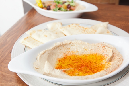 Plate of hummus covered with oil that has a salad in the backgroundの写真素材