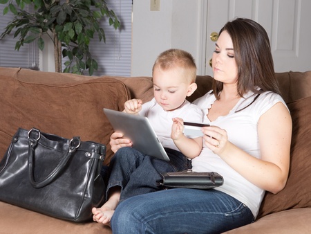 Young mother shopping from conveience at home on tablet with toddler sonの写真素材