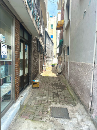 A bright and narrow back alley between buildings in an urban residential area, paved with weathered bricks and lined with air conditioning units, glass windows, and miscellaneous oの写真素材