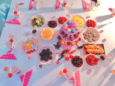 Overhead view of a festive bridal shower table filled with colorful desserts, macarons, fruit, snacks, and drinks, arranged for a joyful party celebration.の写真素材
