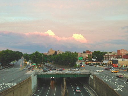 Soft clouds glow in the evening sky as cars travel beneath the overpass in a vibrant city scene. A tranquil pause amid the urban rush hour.の写真素材