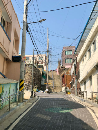 A steep alleyway in a Korean residential neighborhood, with narrow sidewalks, overhead wires, and urban textures. A glimpse into local everyday life.の写真素材