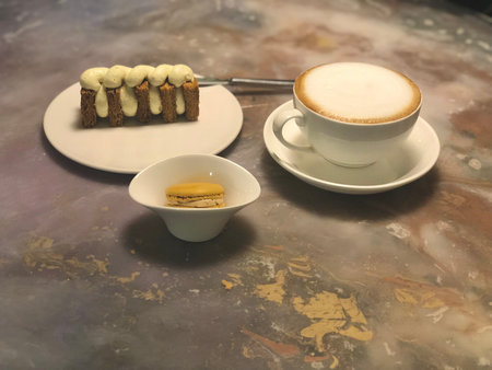 A warm and inviting cafe table featuring a foamy cappuccino, a creamy mille-feuille pastry, and a yellow macaron. The marble-textured table adds an artistic touch, making it a perfの写真素材