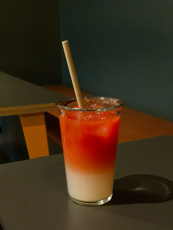 A vibrant iced fruit drink with red and white layered gradient colors, served in a clear glass with a paper straw on a modern cafe table.の写真素材