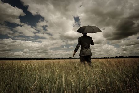Business concept with a man holding an umbrella as a storm approaches.の写真素材