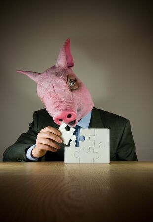 A businessman with a (pigs) mask finishing a puzzle.の写真素材