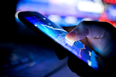 A city businessman using a mobile device to check stocks and market data. Close up shot.