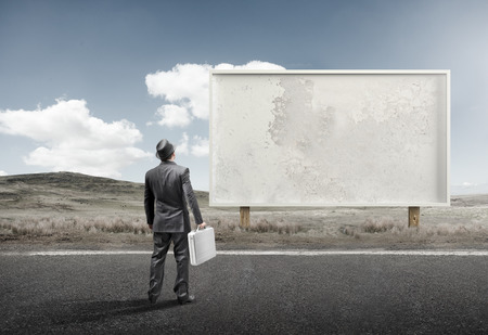 A business man standing and staring at a blank billboard advertisement.の写真素材