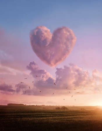 A landscape sunset with a pink fluffyheart shaped cloud. Love and likes concept illustration.の写真素材