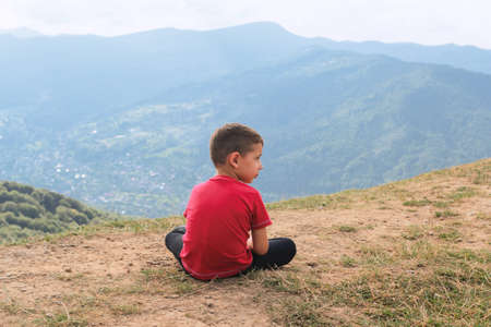 Little boy is sitting in nature. Hiking among hills and forests.の写真素材