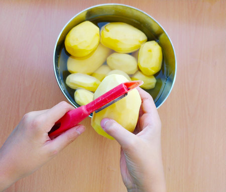 Man holding and peeling potatoes. Hands cutting potatoes at kitchen to prepare a recipe.の写真素材