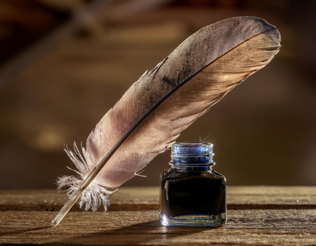 Close-up image of a feather pen next to an ink bottle on a wooden desk, symbolizing writing, creativity, and vintage style.の素材