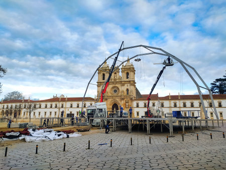 Workers are installing a large steel frame structure in front of Alcobaca Monastery, a historic site, under a cloudy sky in the town's central squareの写真素材