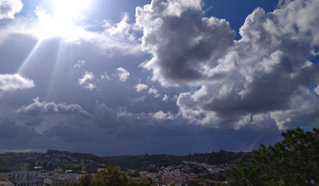 A scenic view of a small town surrounded by lush green hills under a clear blue sky with scattered clouds, showing a mix of buildings and nature in distance.の写真素材