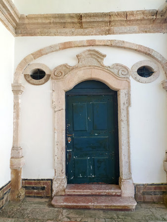 A weathered stone corridor leads to an ornate wooden door framed by intricate arches. Natural light illuminates the walls, showing their textures and details.の写真素材
