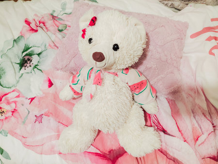 Adorable fluffy white teddy bear in a watermelonprint outfit rests on a pink floral bedspread....