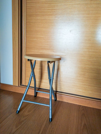 Compact, lightweight, foldable stool with a light wood top and silver frame. Perfect for small spaces, extra seating, or as a side table. Ideal for home, office, or travel.の写真素材