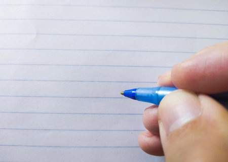 Closeup of a hand holding a blue pen above lined paper. Perfect for concepts of writing, education, notetaking, or backtoschool themes.の写真素材