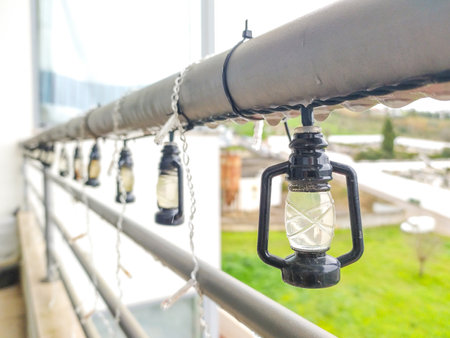 Charming miniature lantern string lights adorn a balcony railing on a rainy day. Perfect for blogs, websites, or adding a touch of cozy ambiance to your designs. Ideal for autumn or winter themes.の写真素材