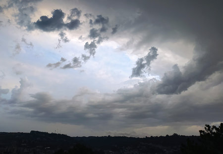 Rich layers of clouds gather over a hillside town in the late afternoon, as beams of sunlight break...