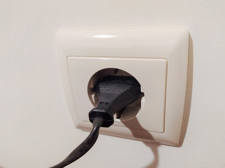 Closeup of a black electrical plug inserted into a creamcolored wall socket. Simple, clean image...