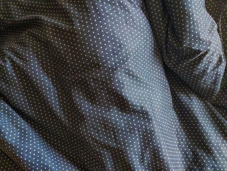 Closeup texture of dark fabric with small, light dots. Softly wrinkled material showing subtle...