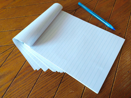 Blank lined notepad and blue pen rest on a rich woodgrain surface. Perfect for concepts of writing,...