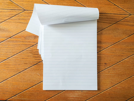 Blank lined notepad rests open on a rich, brown wood grain surface. Perfect for education, office, or stationery designs. Simple, clean aesthetic ideal for mockups backgrounds.の写真素材