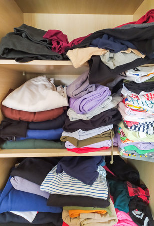 Overstuffed wardrobe shelves overflowing with neatly folded and casually piled clothing. A visual...