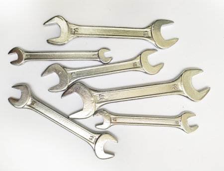 A collection of shiny metal wrenches scattered on a white background. This image conveys concepts of...