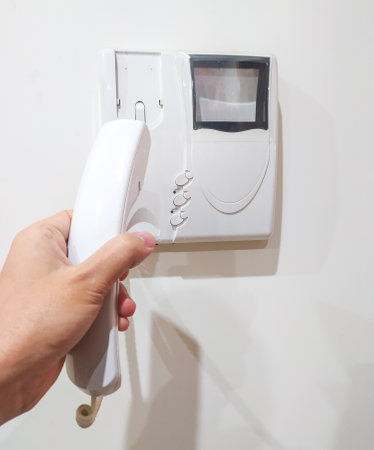 Hand holding intercom phone, security concept. Calling for assistance, receiving visitors. Use for...