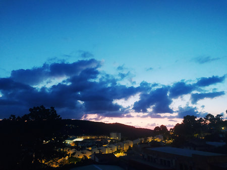 Dramatic twilight landscape featuring a small town nestled beneath a silhouette of hills, and a...
