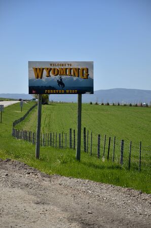 Road sign indicating entry into the state of wyoming, United States of America. In the background blue sky and green grass fied.の写真素材