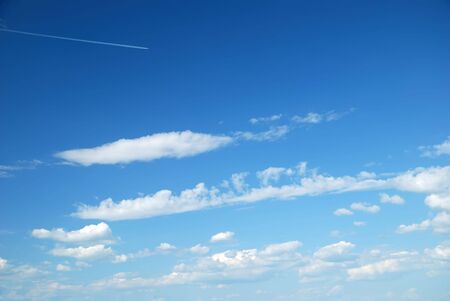 Fantastic soft white clouds against blue sky and far flying airplaneの写真素材