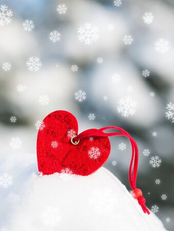 red heart toy in snowfall on fir treeの写真素材