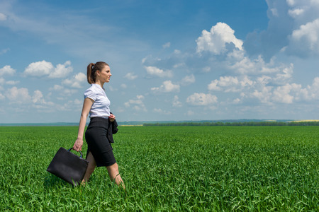 girl with a briefcase walking on green grass fieldの写真素材