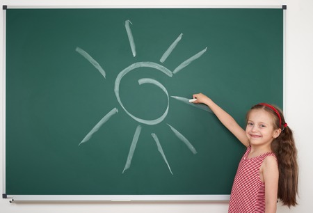 girl drawing sun by white chalk on school boardの写真素材