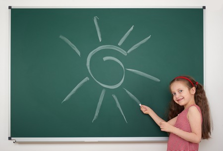 girl drawing sun by white chalk on school boardの写真素材